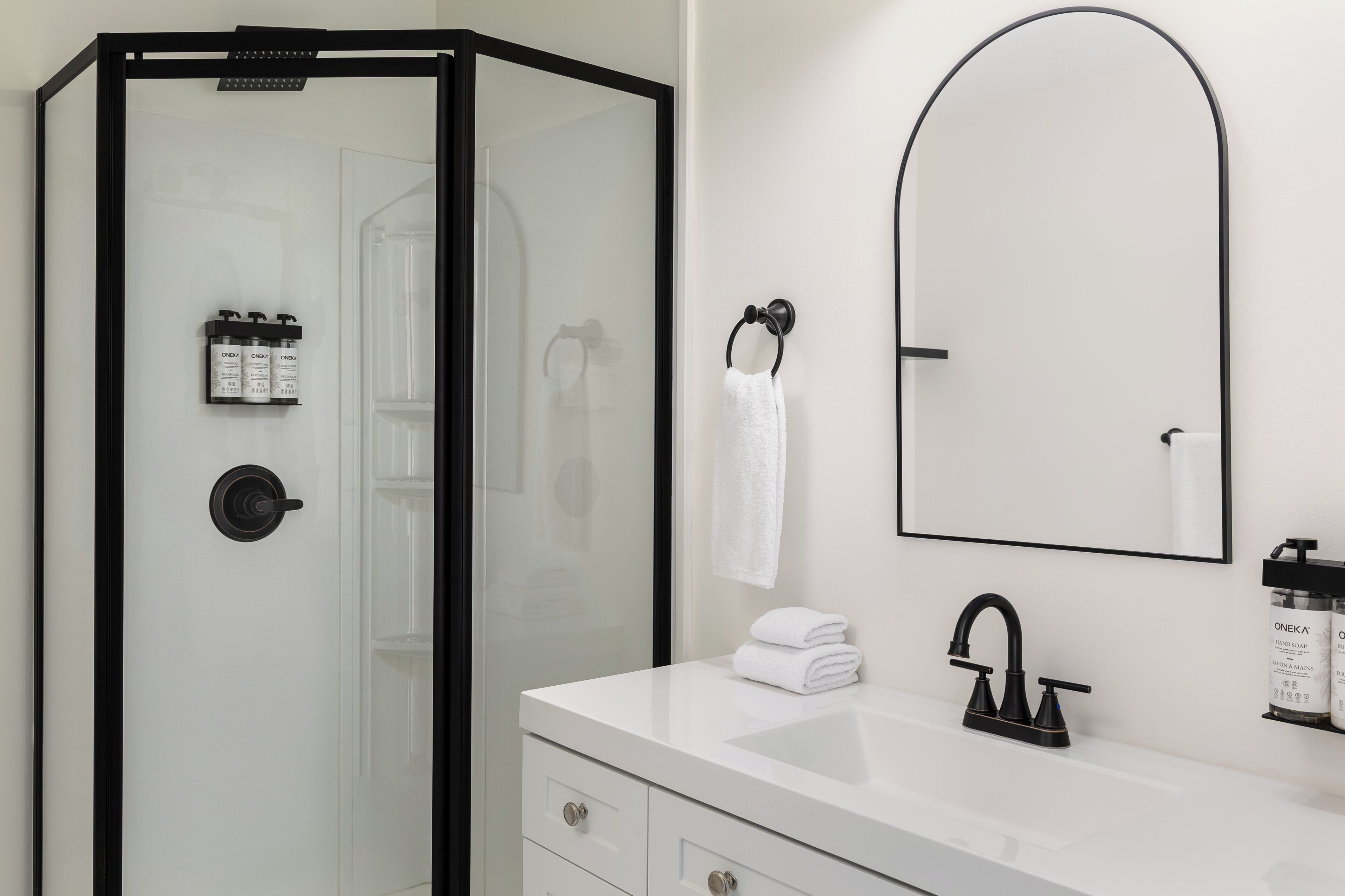 A modern bathroom with a glass-enclosed shower, a white sink with a black faucet, and toiletries on the wall.