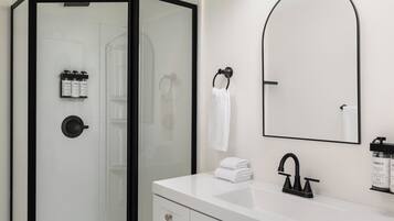 A modern bathroom with a glass-enclosed shower, a white sink with a black faucet, and toiletries on the wall.