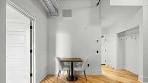 Una habitación moderna y luminosa, con piso de madera, paredes blancas y una mesa central con sillas.