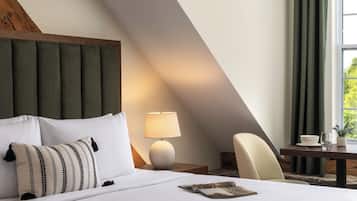 Habitación de hotel con cama, mesita de noche, lámpara, silla y ventana con cortinas.