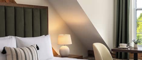 Une chambre d’hôtel avec un lit, une table de chevet, une lampe, une chaise et une fenêtre avec des rideaux.