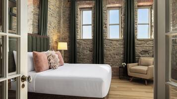 A bedroom with a stone wall, a bed with white bedding, a green headboard, and a small table with a lamp.