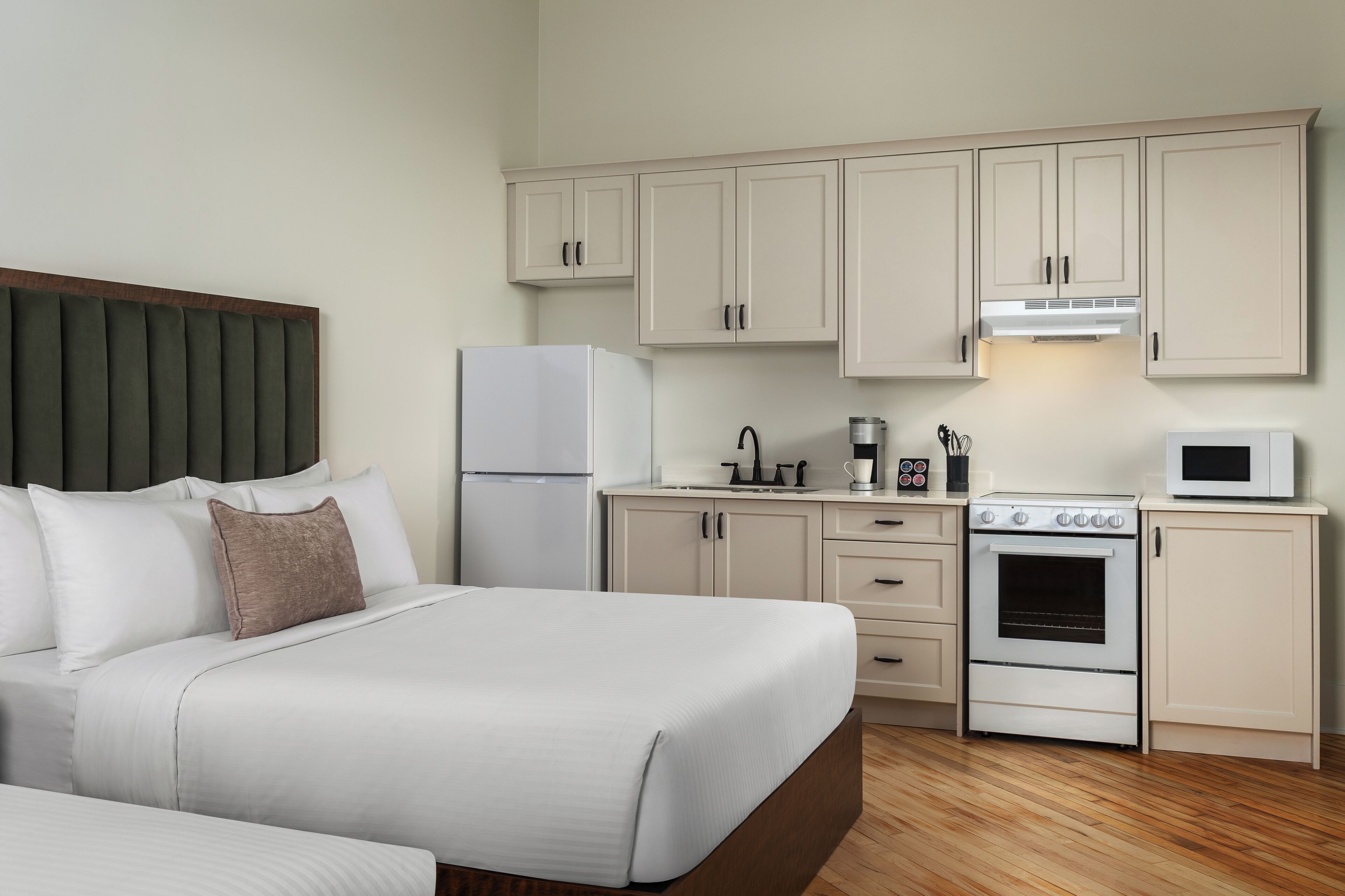 Una habitación de hotel con una cama, un kitchenette y piso de madera.