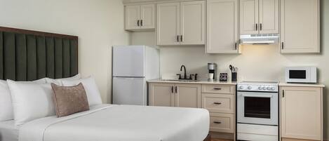 A hotel room with a bed, a kitchenette, and a wooden floor.