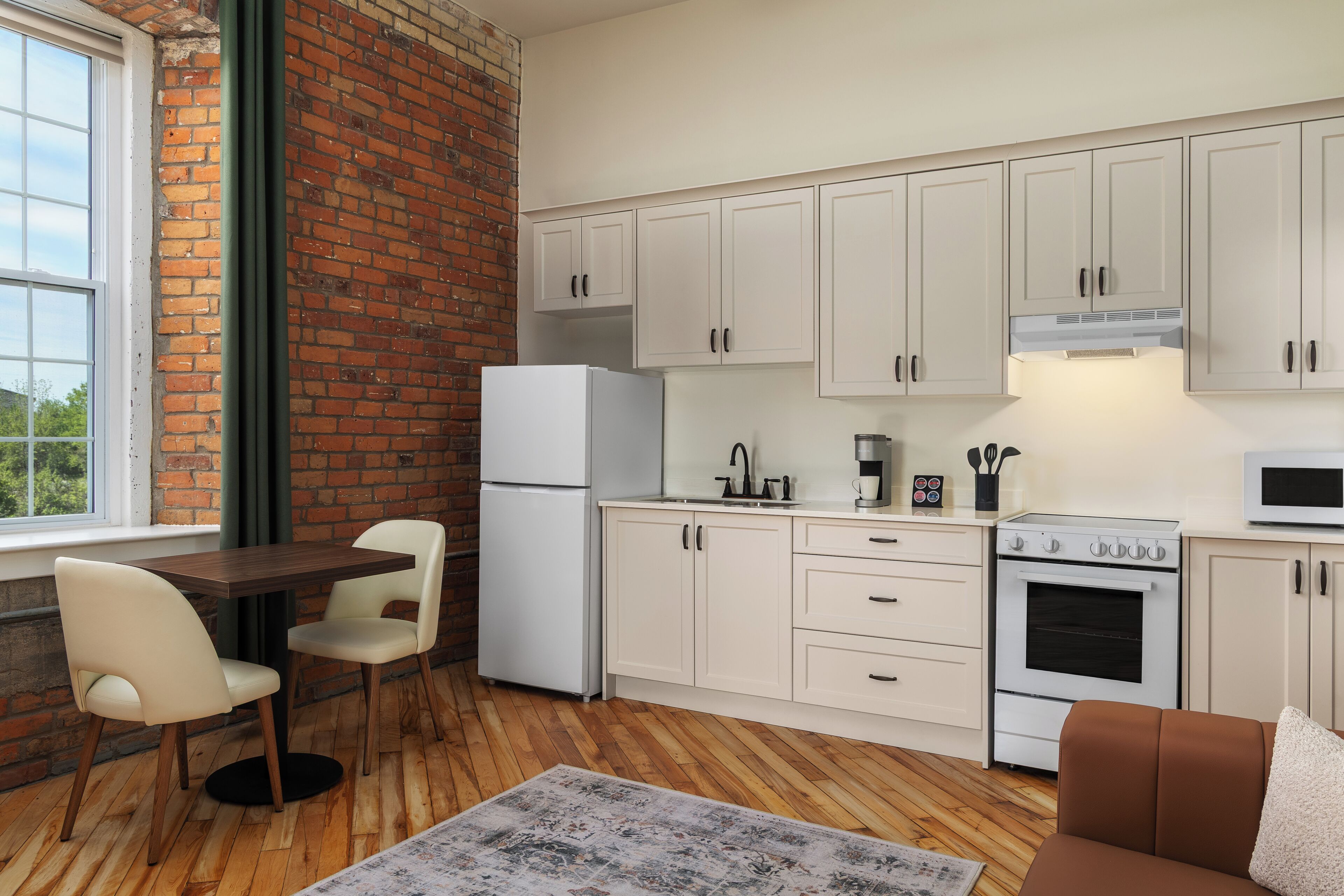 A compact kitchen with white cabinets, a refrigerator, a stove, and a microwave. There's a dining area with a table and chairs.