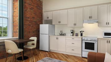 A compact kitchen with white cabinets, a refrigerator, a stove, and a microwave. There's a dining area with a table and chairs.