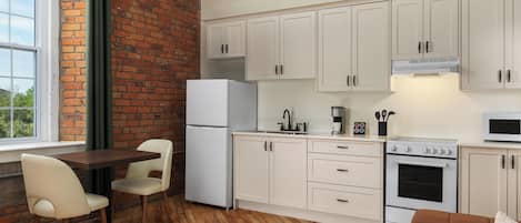 A compact kitchen with white cabinets, a refrigerator, a stove, and a microwave. There's a dining area with a table and chairs.