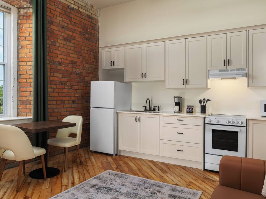 A compact kitchen with white cabinets, a refrigerator, a stove, and a microwave. There's a dining area with a table and chairs.