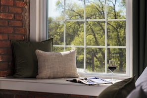 Asiento junto a la ventana con un cojín, una copa de vino tinto y una revista.