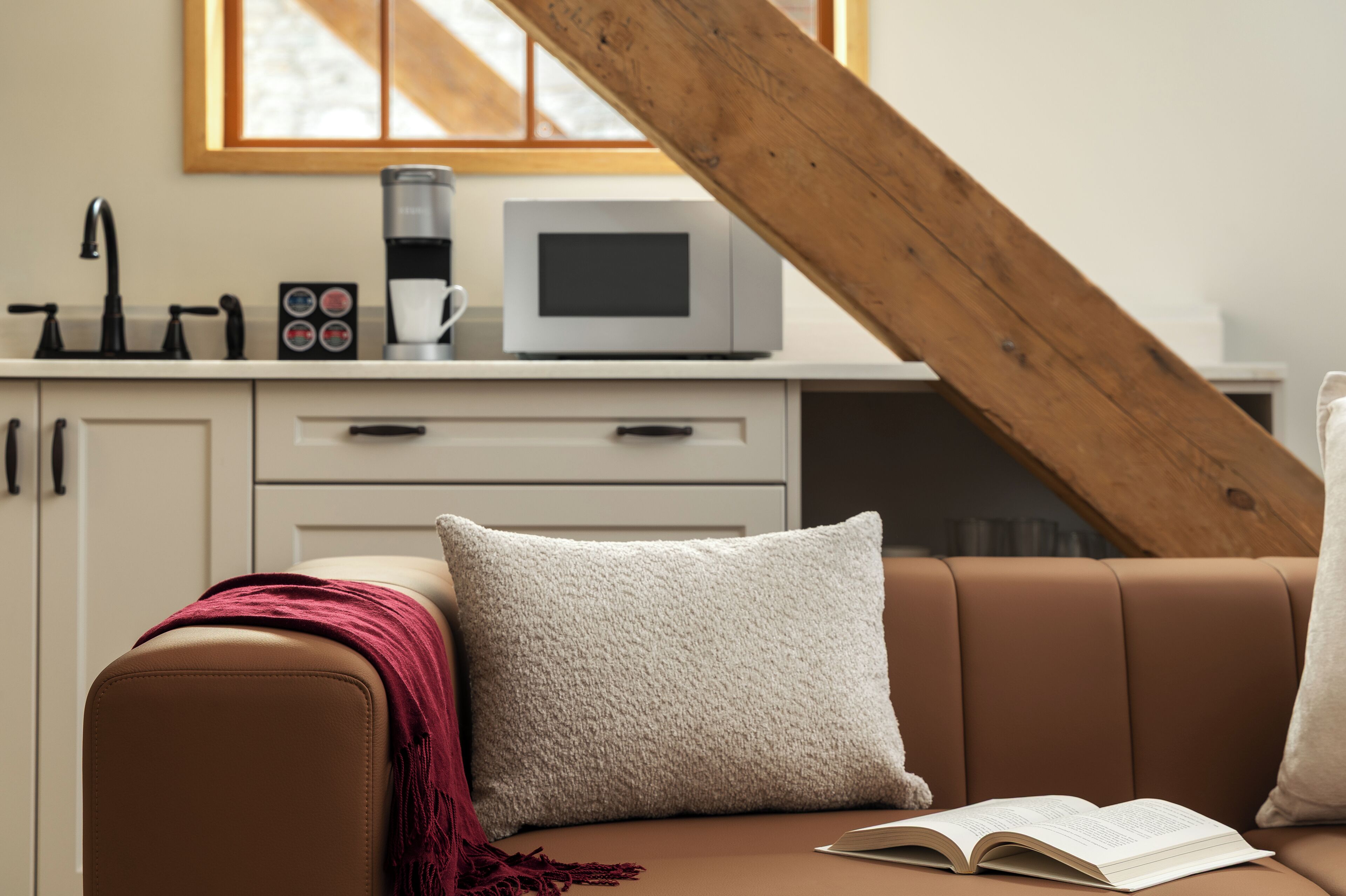 Un salon chaleureux avec un canapé en cuir marron, un coussin blanc et un livre posé sur l’accoudoir.