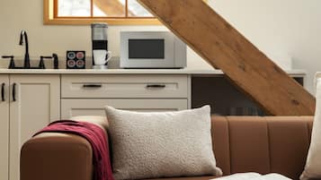 Un salon chaleureux avec un canapé en cuir marron, un coussin blanc et un livre posé sur l’accoudoir.