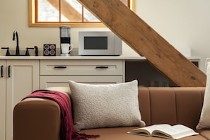 A cozy living room with a brown leather sofa, a white throw pillow, and a book on the armrest. - Tri Century Mill Suites (Carleton Place)