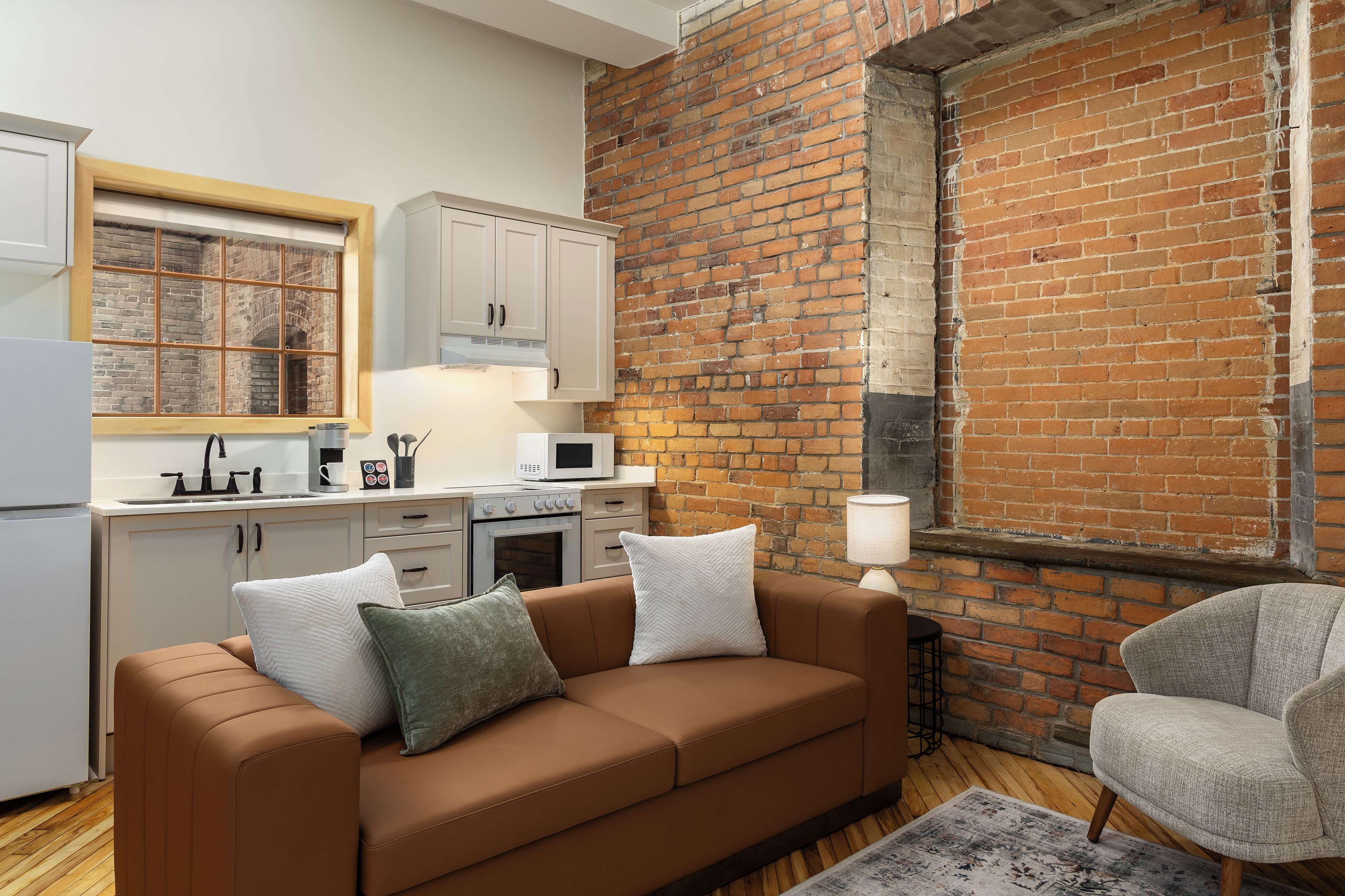 A modern kitchen with white cabinets, a brown leather sofa, and a brick wall.