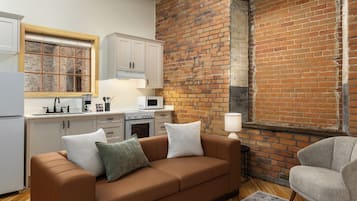 A modern kitchen with white cabinets, a brown leather sofa, and a brick wall.