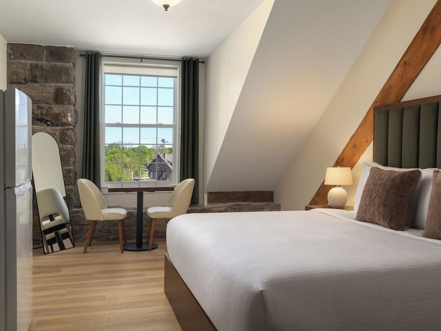 A hotel room with a bed, a desk, a chair, a window, and a stone wall.