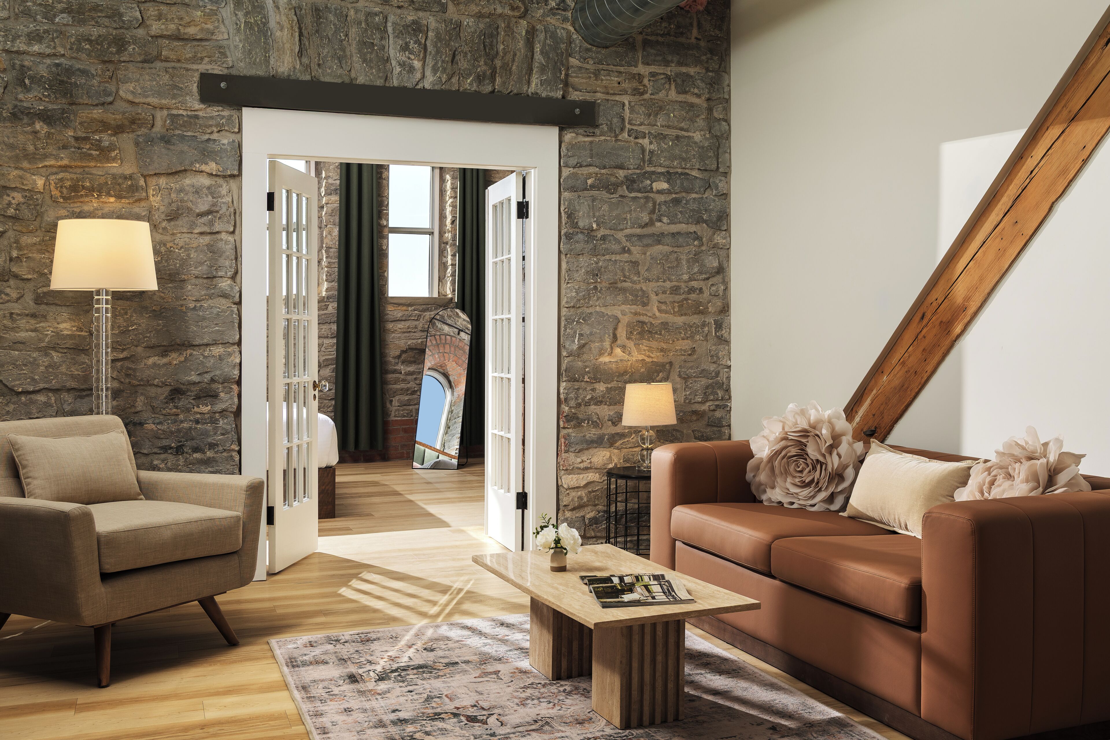 A modern living room with a stone wall, a brown leather sofa, a beige armchair, a coffee table, and a lamp.