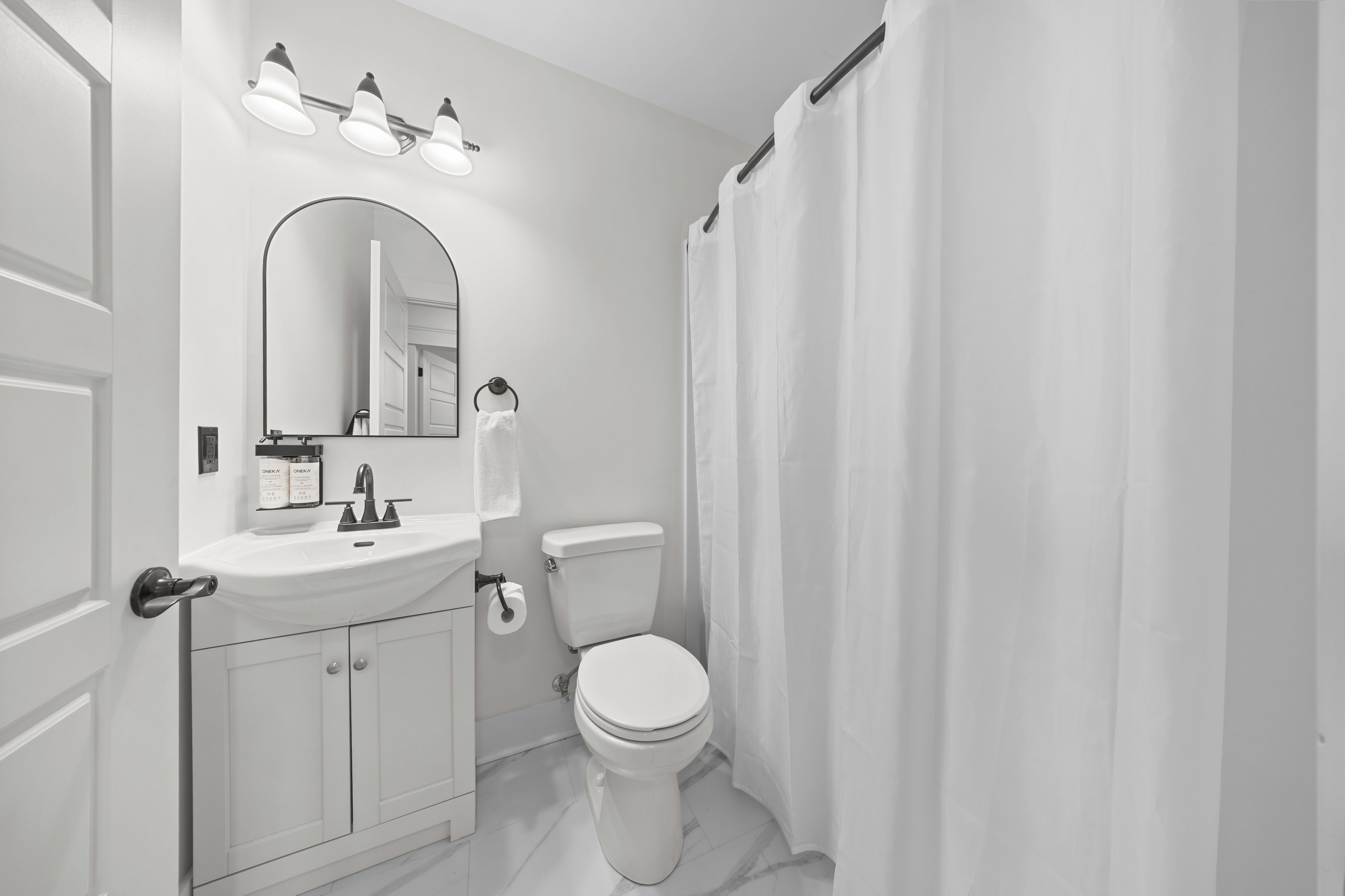 A bathroom with a white sink, mirror, and toilet. There are three lights above the mirror and a shower curtain.