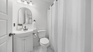A bathroom with a white sink, mirror, and toilet. There are three lights above the mirror and a shower curtain.