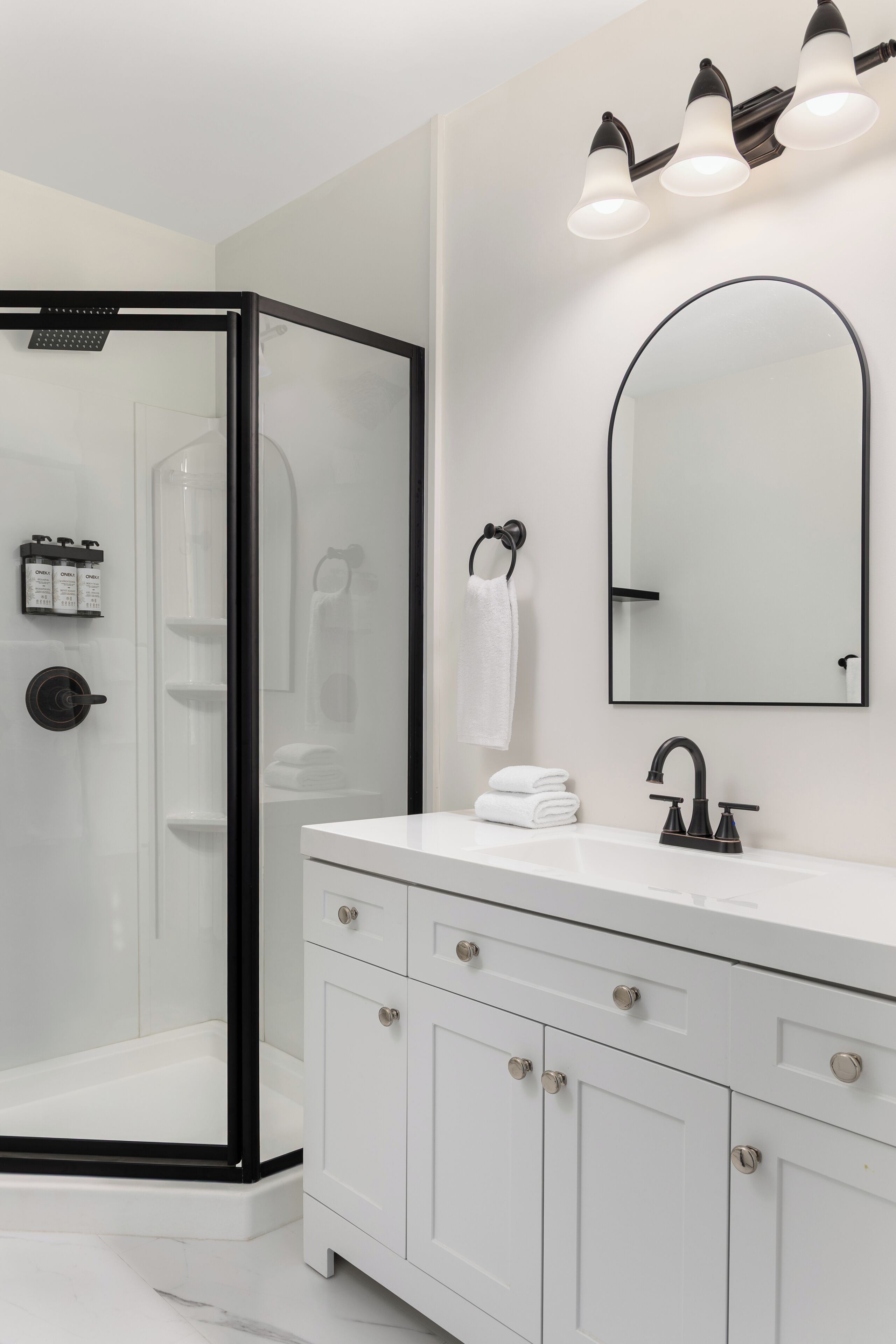 A modern bathroom with a glass shower enclosure, a white vanity with a black faucet, and a large mirror above the sink.