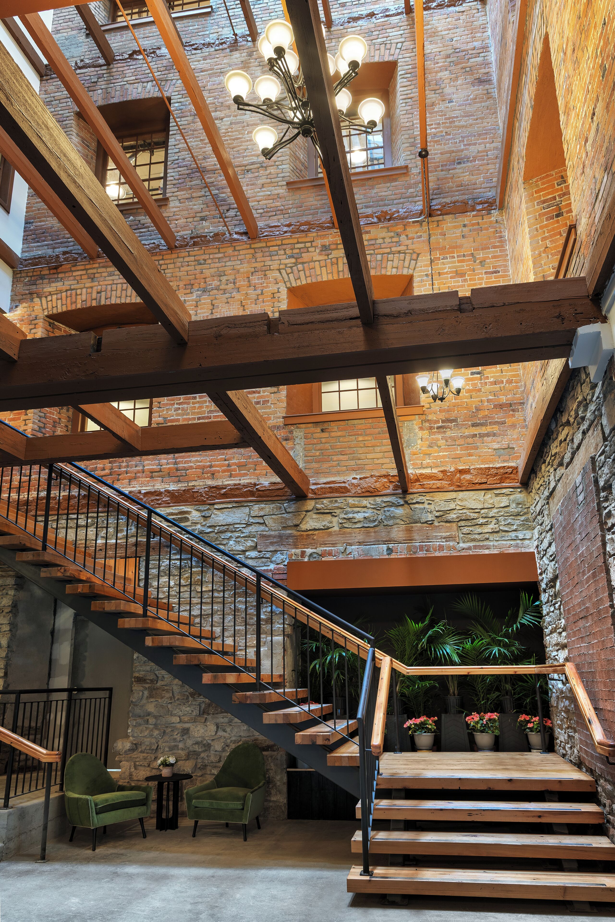 A spacious interior with exposed brick walls, a wooden staircase, and a modern chandelier.