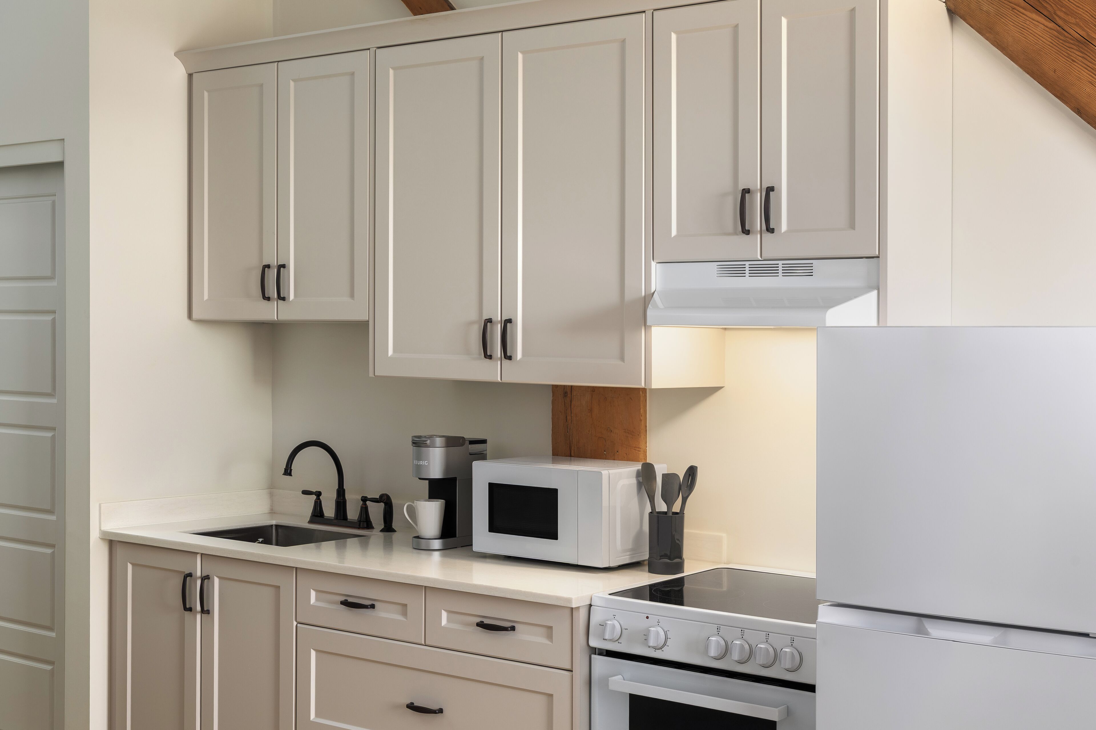 A kitchen with white cabinets, a coffee maker, a microwave, a stove, and a refrigerator.