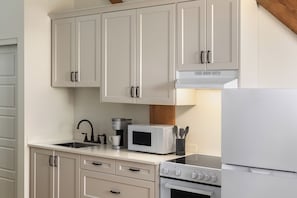 A kitchen with white cabinets, a coffee maker, a microwave, a stove, and a refrigerator. - Tri Century Mill Suites (Carleton Place)