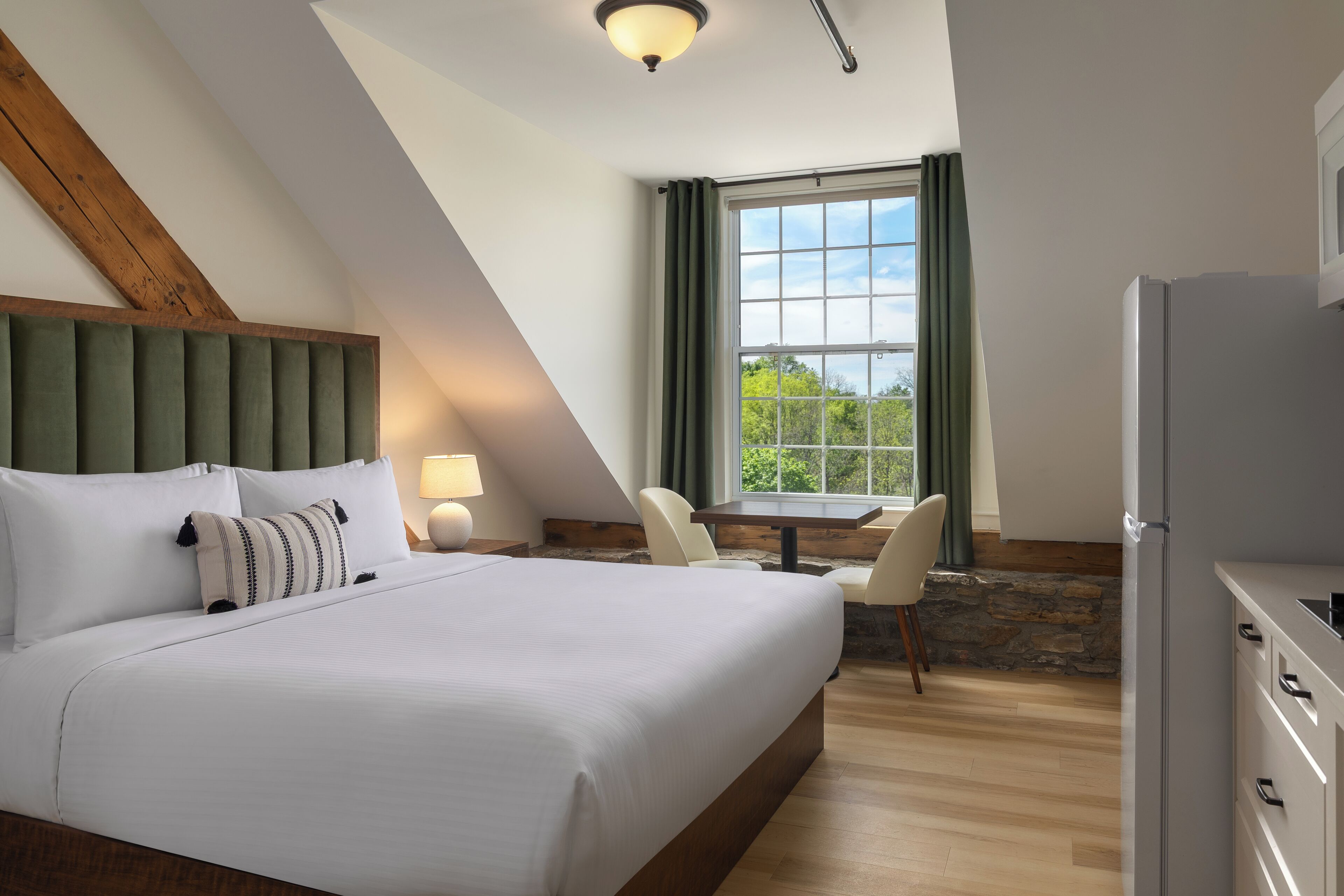 A modern hotel room with a large bed, a desk, and a window with curtains.