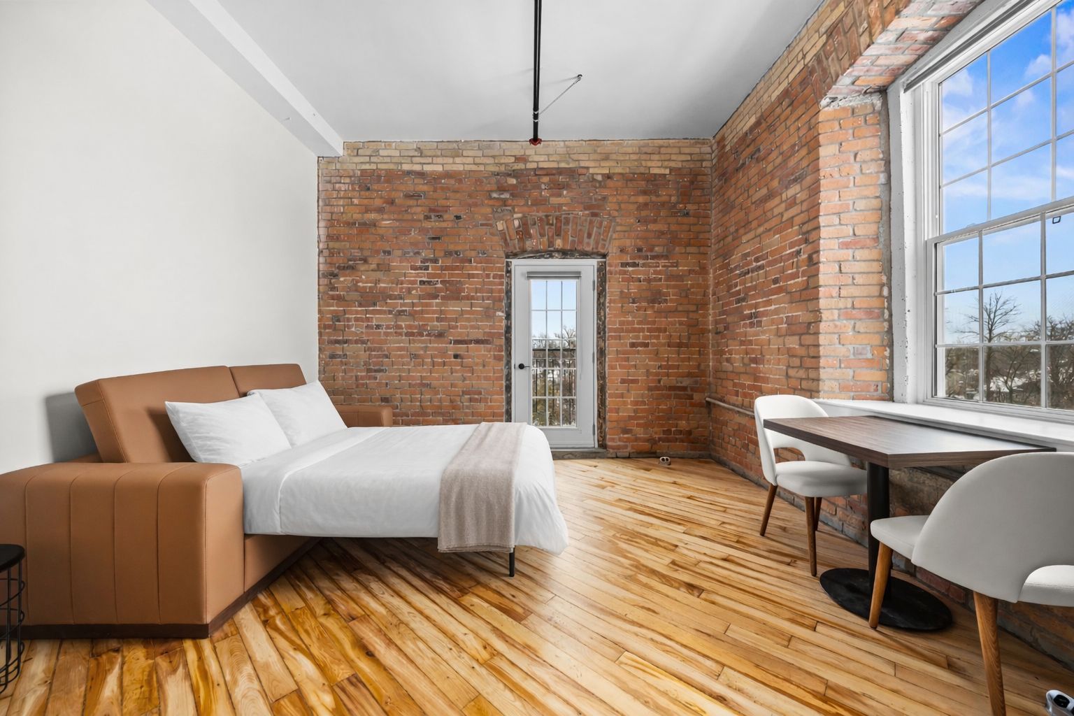 Un dormitorio moderno con pared de ladrillo, suelo de madera, cama, sofá, mesa y silla.