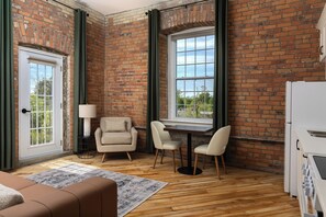 A room with a brick wall, a large window, a sofa, a table, and chairs. - Tri Century Mill Suites (Carleton Place)