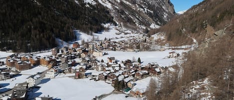 A snow-covered village with traditional buildings, a clear sky, and mountains in the background.