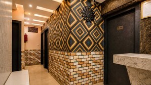 A hallway with patterned walls, a clock, a fire extinguisher, and a reception desk. - SABA GUEST HOUSE (Kolkata)