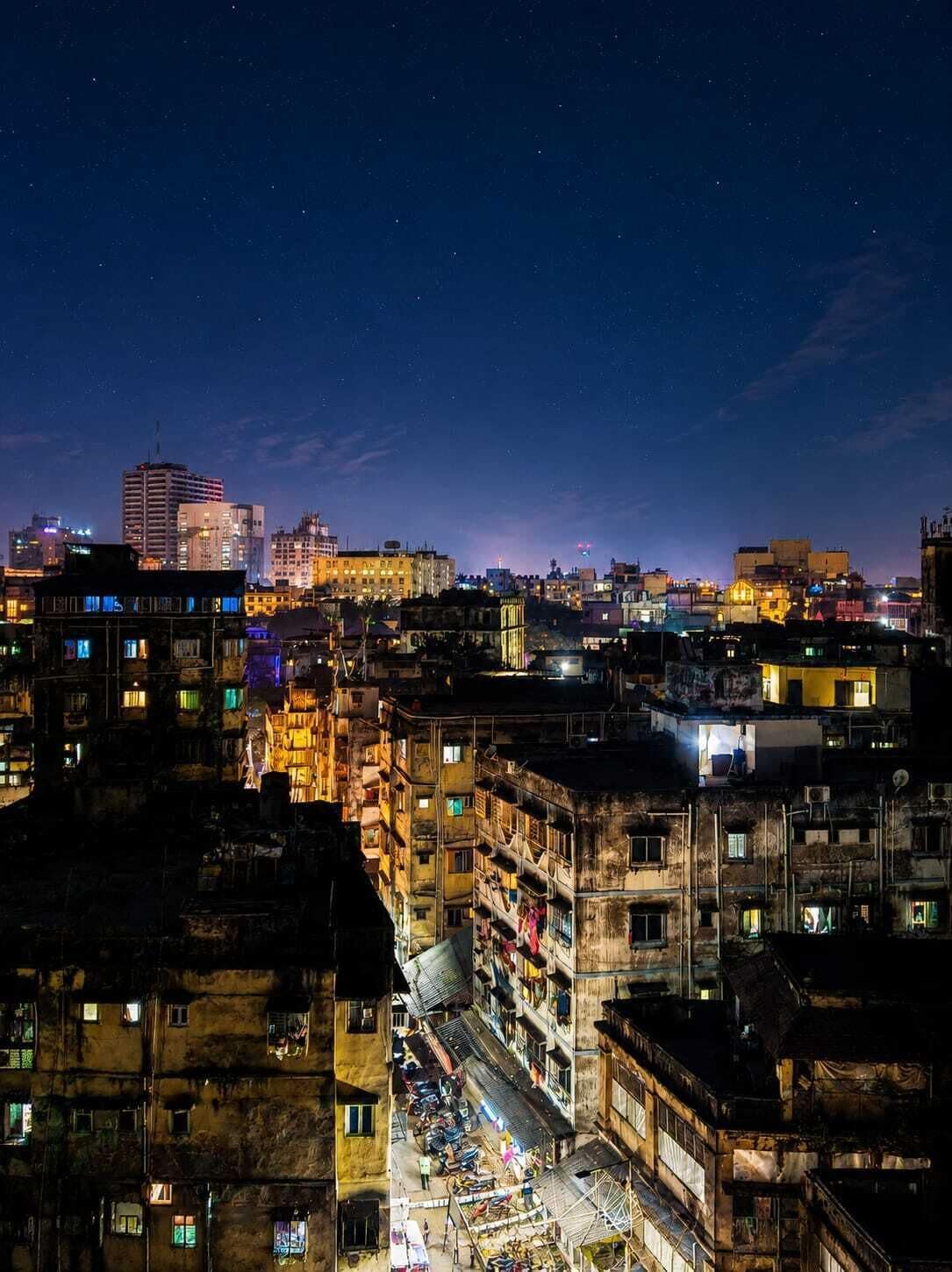 A densely packed urban area at night with illuminated buildings and a clear sky.