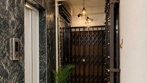 A hallway with a marble wall, a digital elevator control panel, a potted plant, a ceiling light fixture, and a decorative metal gate. - SABA GUEST HOUSE (Kolkata)
