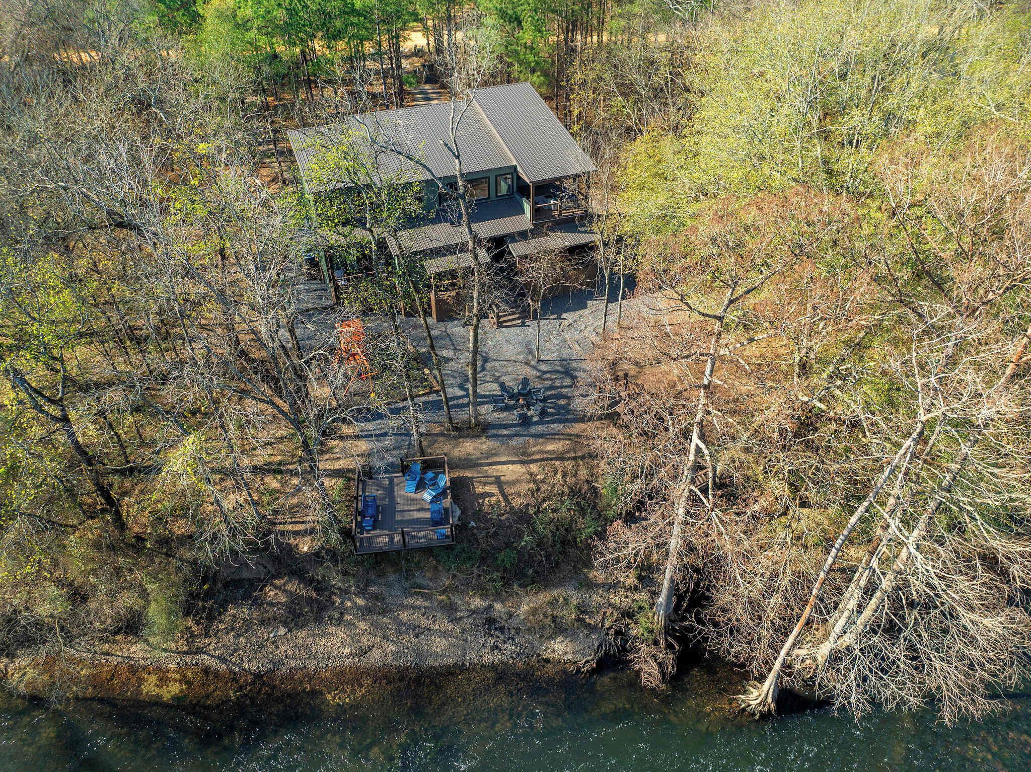 A cabin with a metal roof, surrounded by dense forest and a body of water.