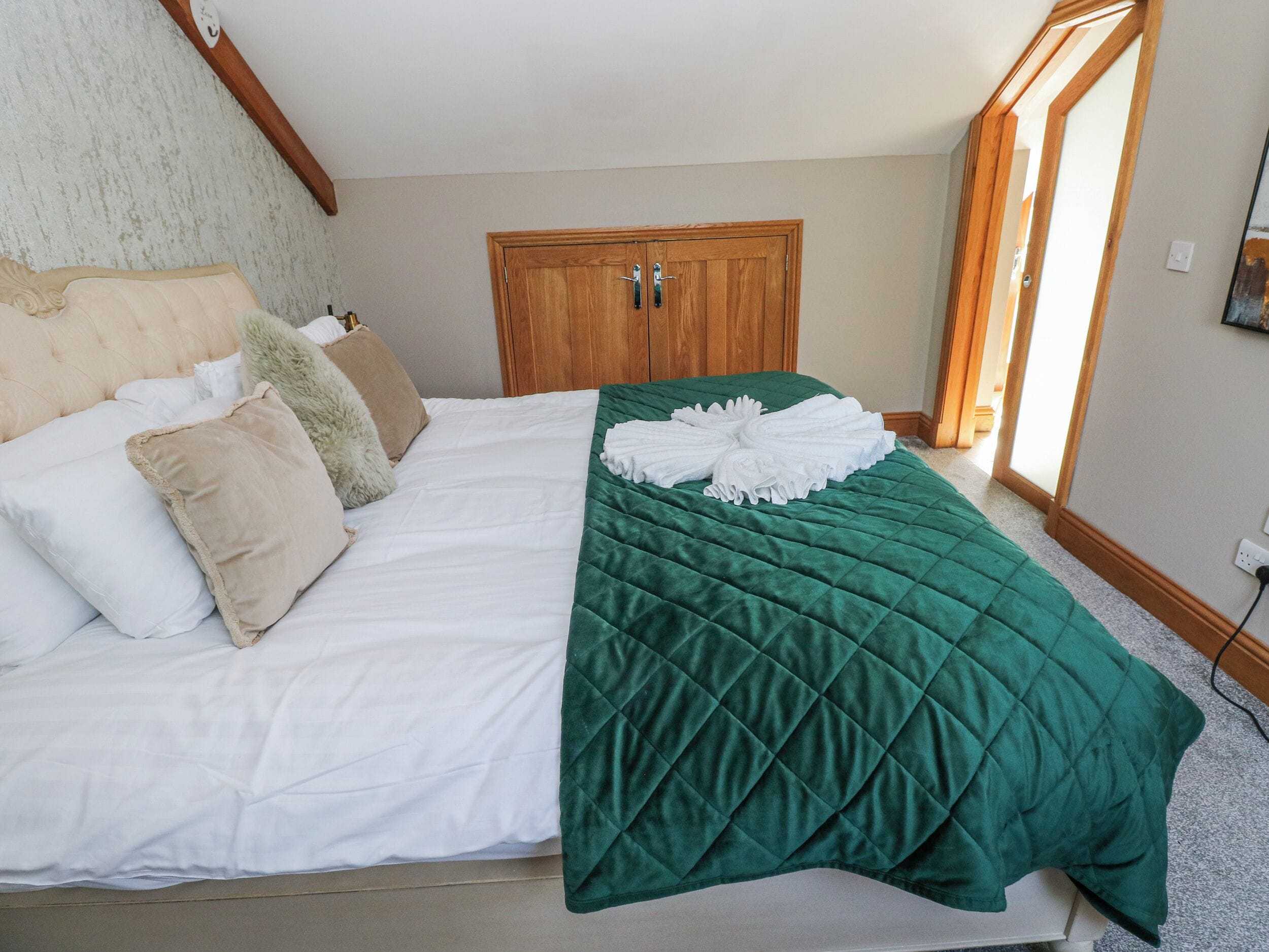 Cama bem arrumada com um edredom verde, travesseiros brancos e uma toalha branca.