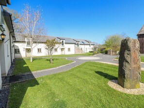 A courtyard with a stone monument, a small tree, and a building with a stone facade and a door. - Rose Apartment - Gower (Swansea)