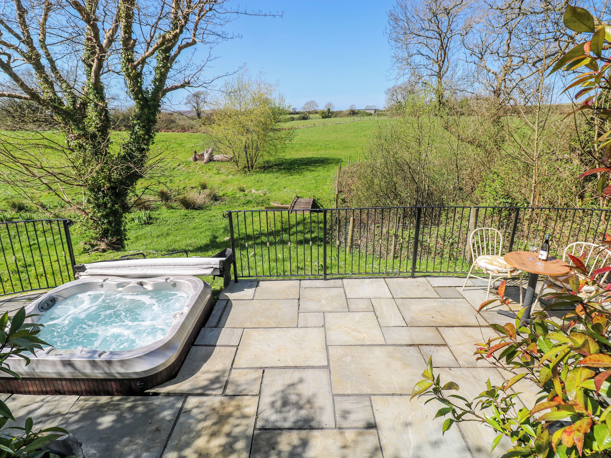 Un bain à remous sur une terrasse en pierre, avec vue sur un champ verdoyant et des arbres.