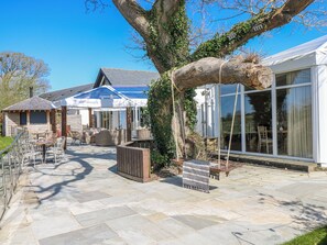 A patio area with outdoor seating, a large tree, and a building with large windows. - Rose Apartment - Gower (Swansea)