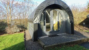 A dome-shaped structure with a glass door, surrounded by gravel and grass, with trees in the background. - Glamping Pod 9 - Gower (Swansea)
