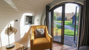 A modern room with a yellow armchair, a small table, and a large sliding glass door leading to an outdoor area. - Glamping Pod 9 - Gower (Swansea)