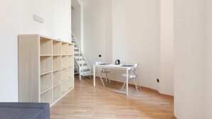 Una habitación con una estantería de madera, una mesa blanca con sillas y una escalera.