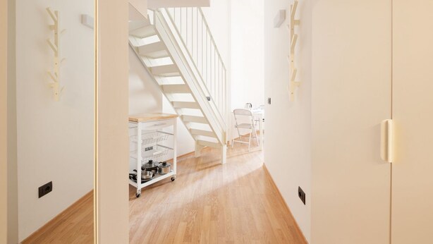 Un pasillo estrecho con suelo de madera, una escalera blanca y un carrito con utensilios de cocina.