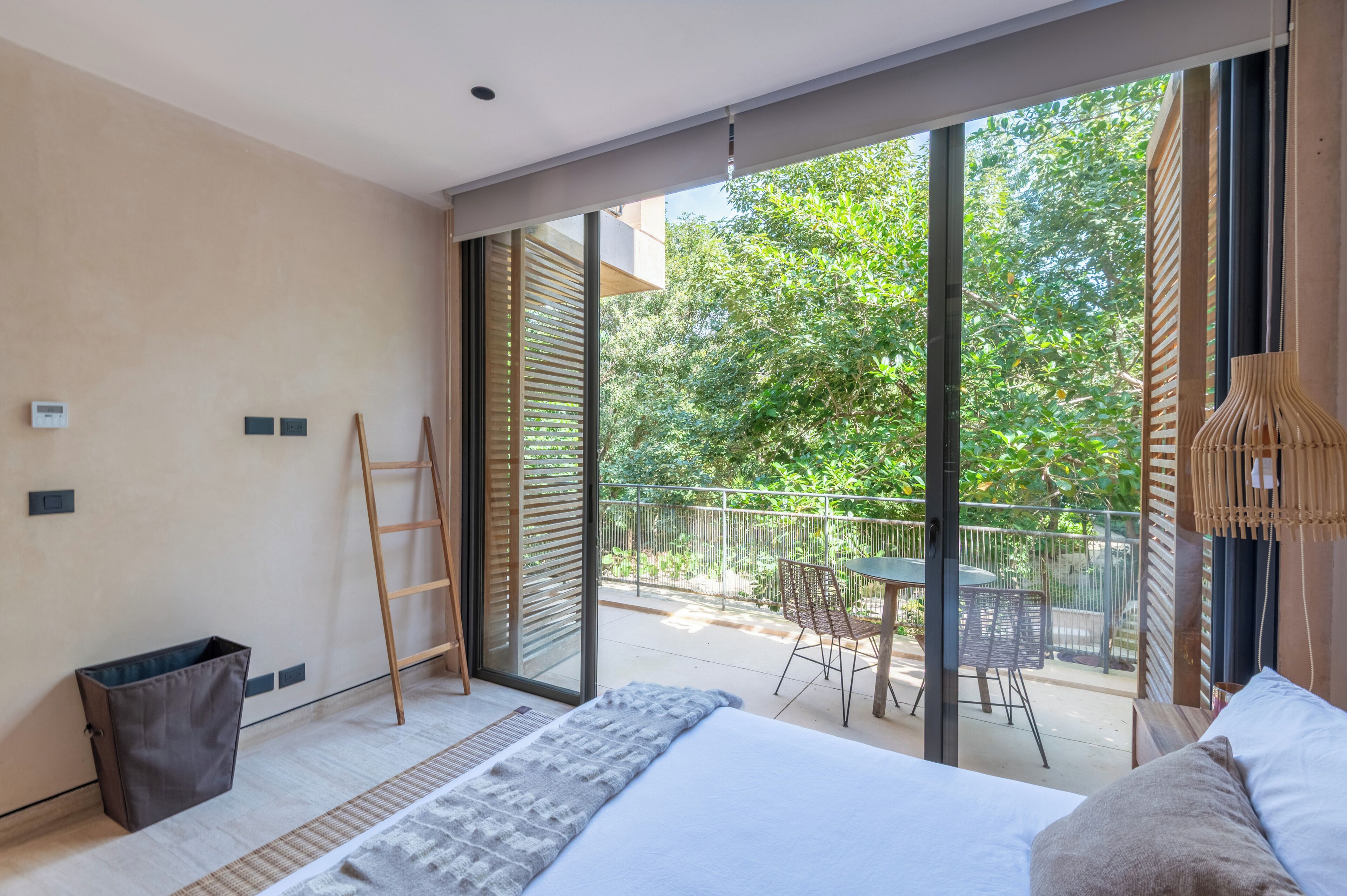 Une chambre moderne avec un grand lit, une vue sur l’extérieur et un balcon aménagé avec du mobilier.