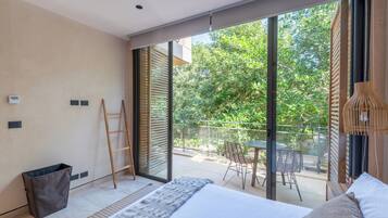 Une chambre moderne avec un grand lit, une vue sur l’extérieur et un balcon aménagé avec du mobilier.