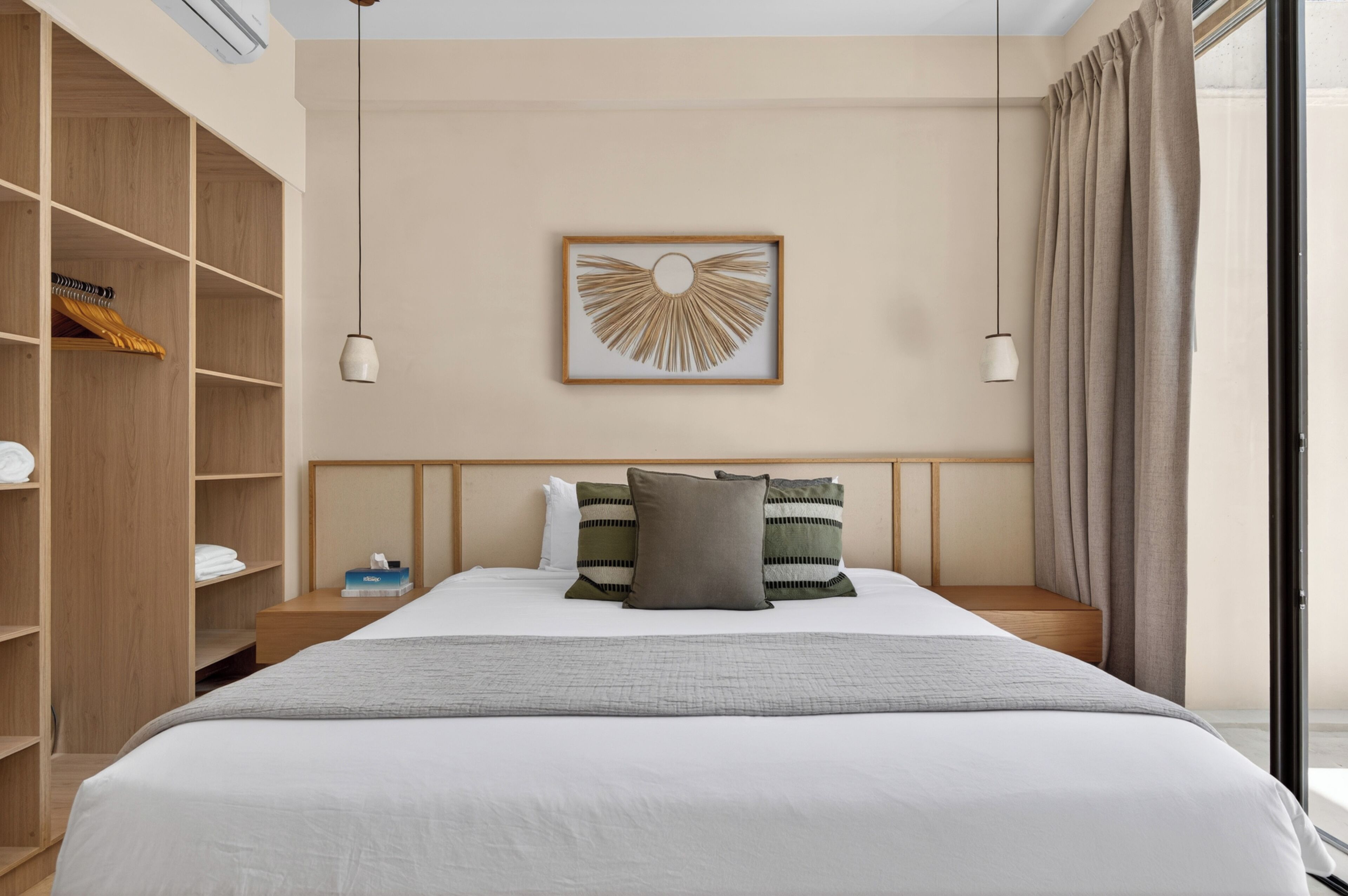 A hotel room with a bed, bedside tables, a wardrobe, a framed artwork on the wall, and a window with curtains.