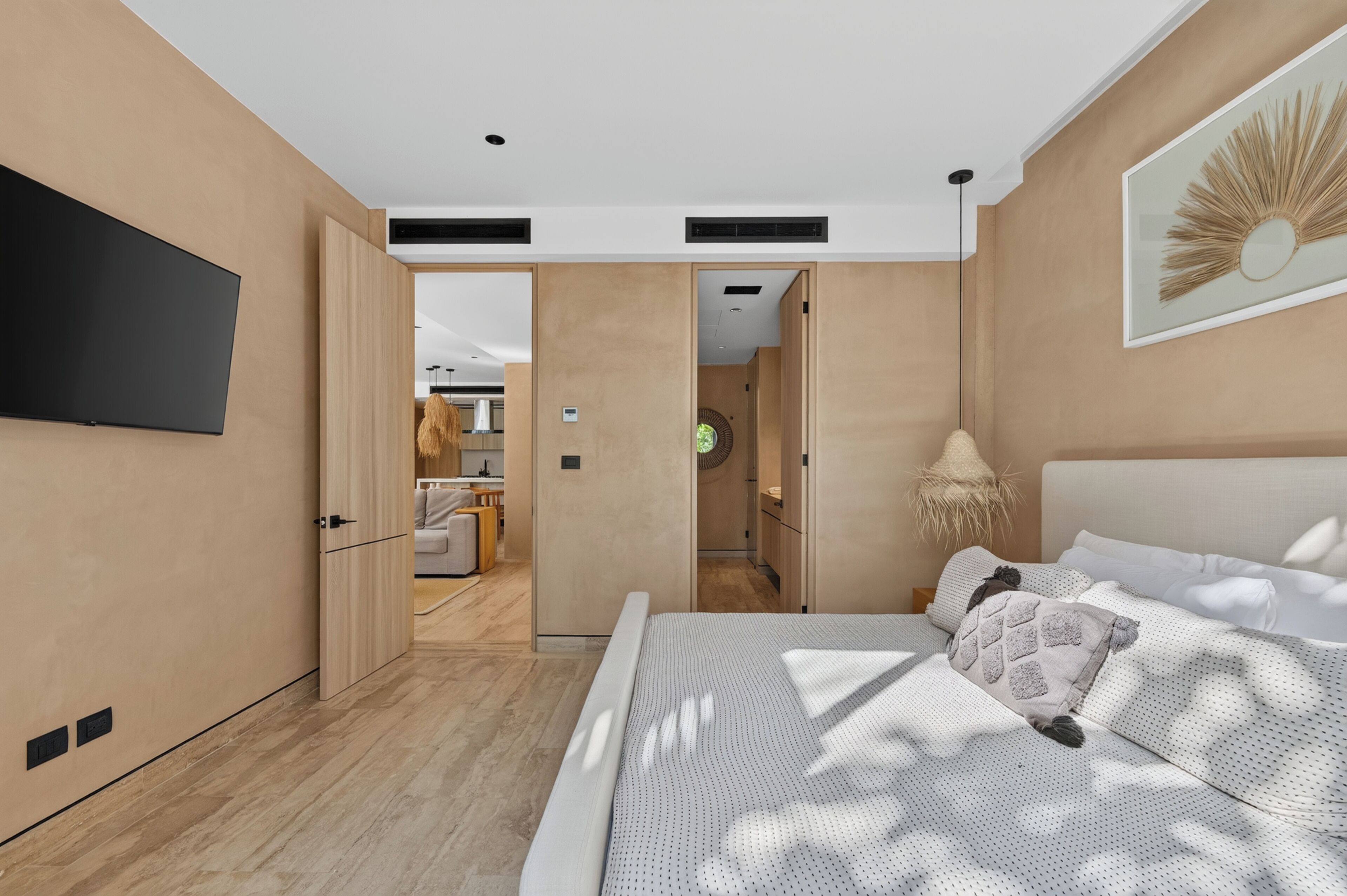 A modern bedroom with a large bed, a flat-screen TV mounted on the wall, and a hallway leading to a bathroom.