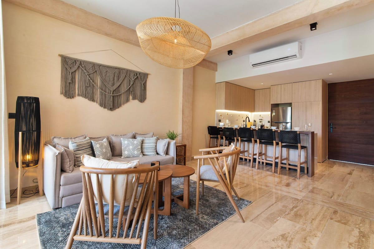 A modern living room with a sofa, wooden chairs, a coffee table, and a hanging light fixture.