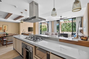 A modern kitchen with a central island, built-in oven, and a dining area with a table and chairs. - Corasol, Relaxed Stay with Terrace &amp; Full Amenities (Playa del Carmen)