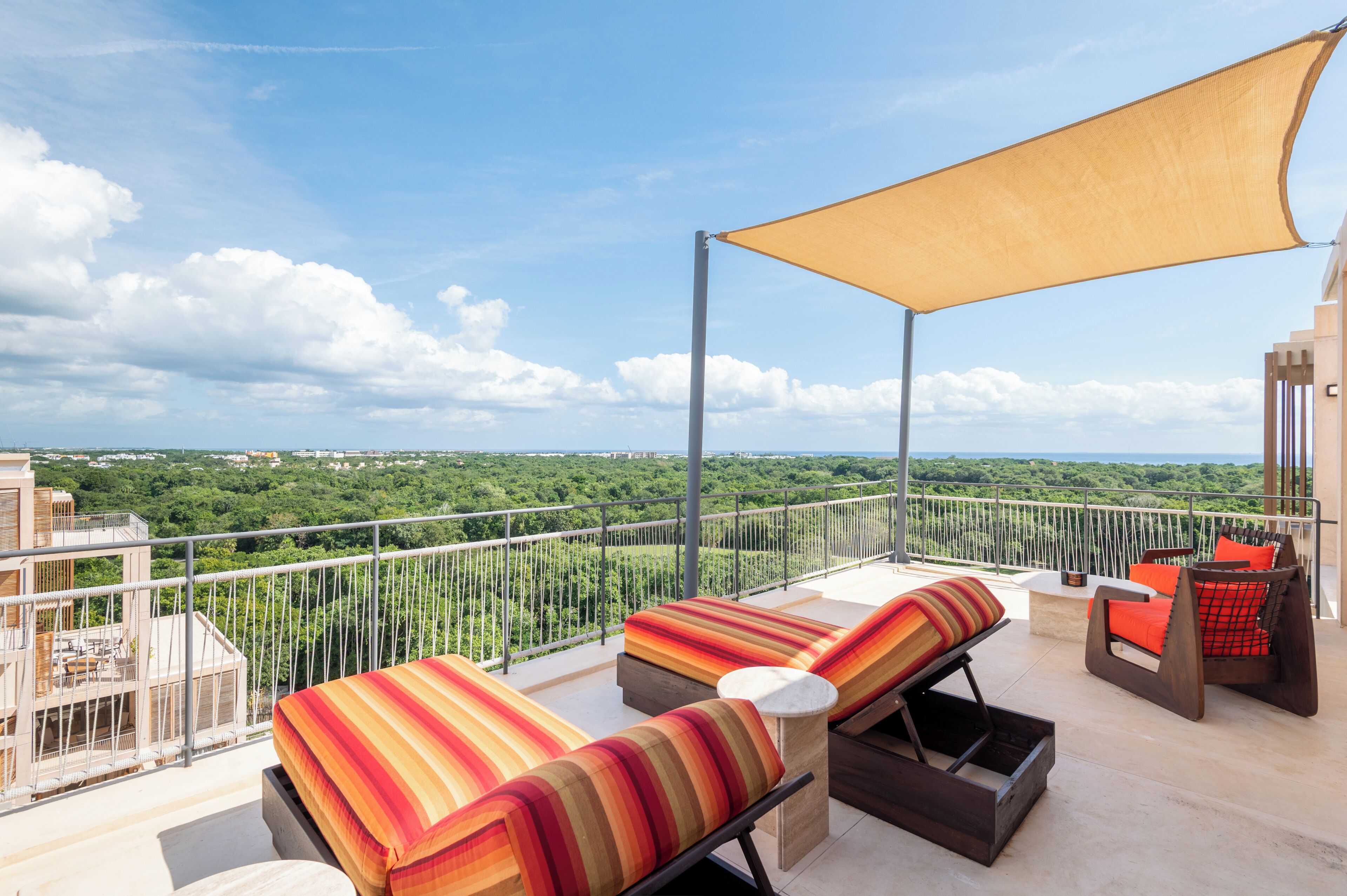 Ein Balkon mit zwei Liegestühlen, einem Tisch und einer großen Markise. Der Balkon bietet Blick auf eine üppige, grüne Landschaft.