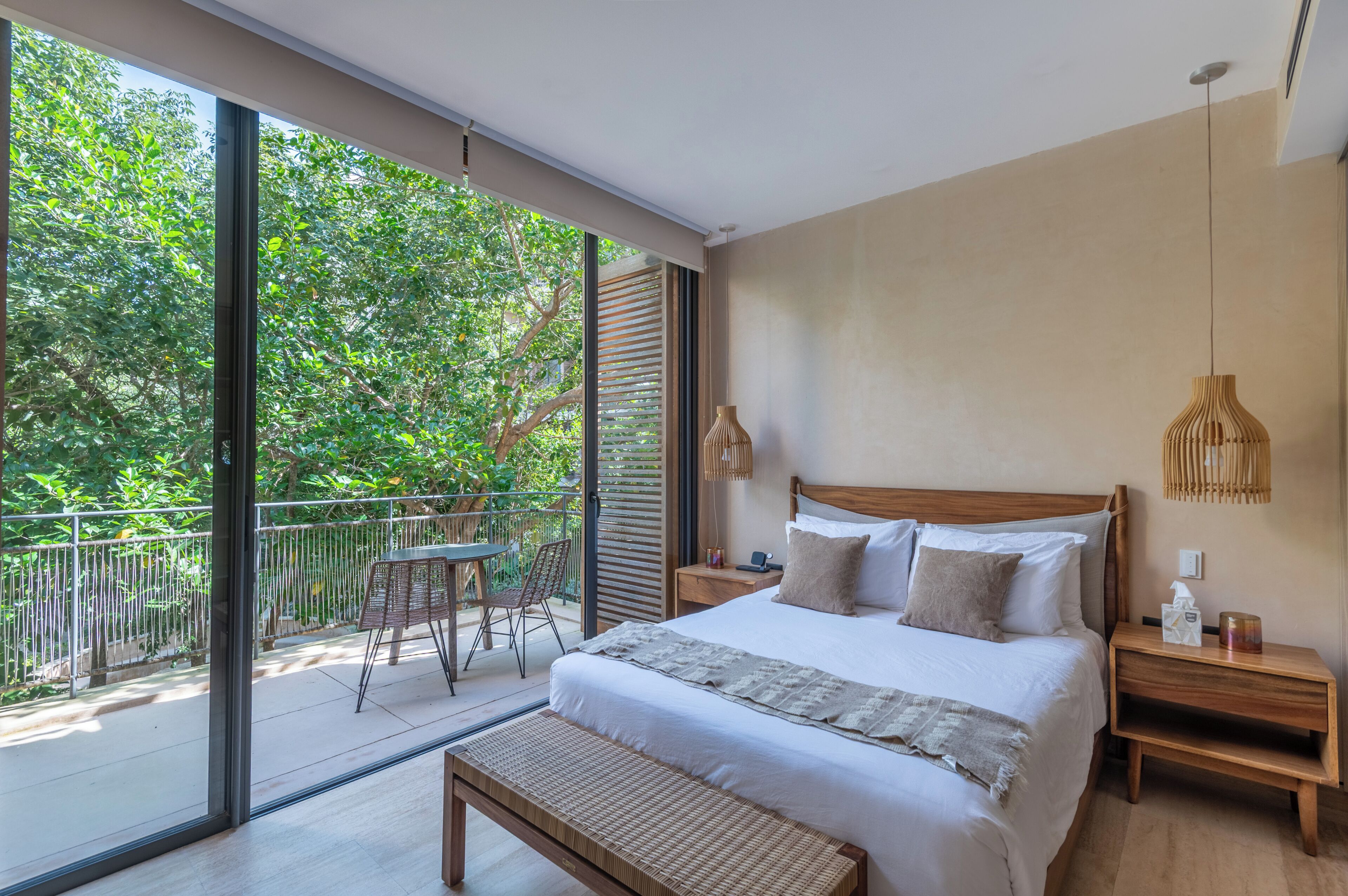 A modern bedroom with a large bed, a wooden nightstand, a bedside table, and a view of a balcony with a table and chairs.